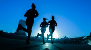 silhouette of three women running on grey concrete road